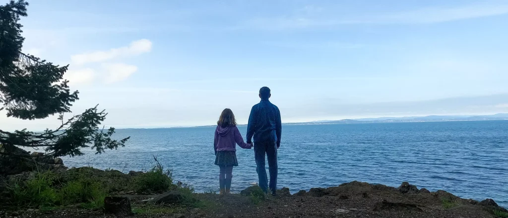Daughter holds her father's hand as they look out over the ocean.