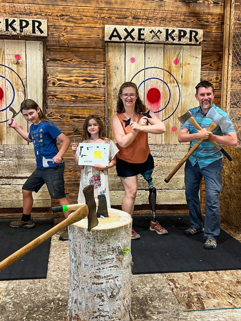 Two adults and one child pose with throwing axes. One child poses with a drawing she made.