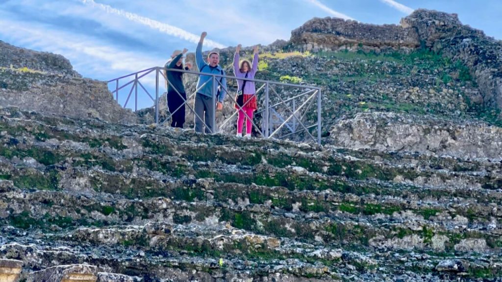 Kids with dad wave from atop the Roman amphitheater in Italica, Spain.